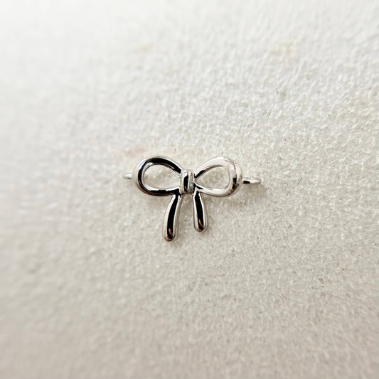 A 9ct white gold bow charm designed for permanent jewellery, delicately attached to a fine chain. The sleek, polished finish catches the light, highlighting the charm’s elegant curves.