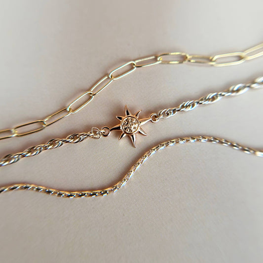 Flat lay of a gold vermeil sun charm paired with a delicate paperclip chain, styled on a neutral background to showcase the warm tones and minimalist elegance of the design.