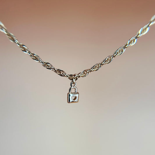 Close-up of a micro-sized 14ct solid gold lock heart drop charm delicately dangling from a solid gold chain, styled to highlight its petite, meaningful design and elegant movement.