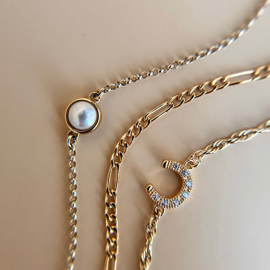 Gold vermeil connector charm with a single pearl, styled on a flat lay background for permanent jewellery.